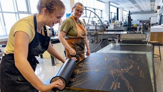 Beth Grabowski smiling and laughing with a student working on an art project.