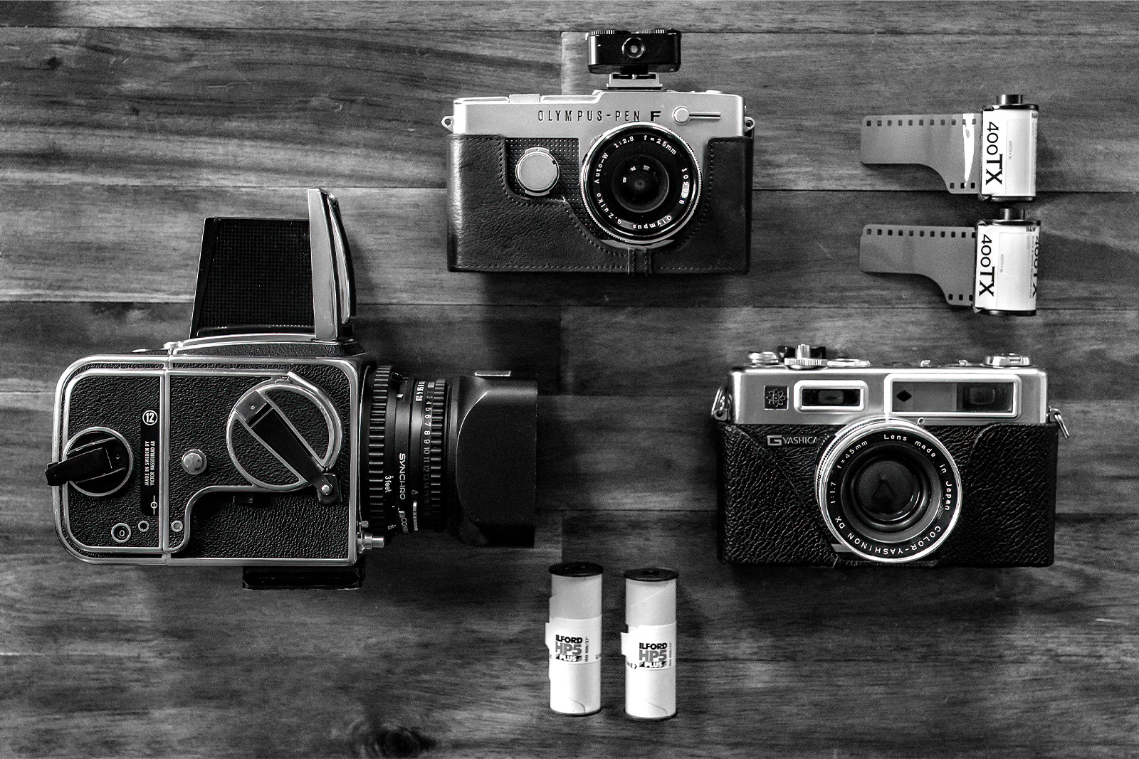 Three cameras sitting on a table: a Hasselblad 500CM medium format camera, an Olympus PEN FV half-frame camera and a Yashica Electro GSN 35 mm camera.