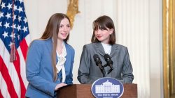 Two students, including UNC-Chapel Hill first-year Kira Tiller on the left, speaking to an audience from a podium inside of a room at the White House.