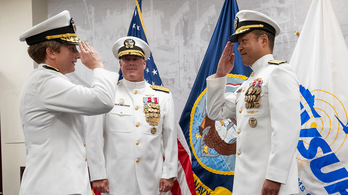 Three individuals in Naval uniforms saluting one another.