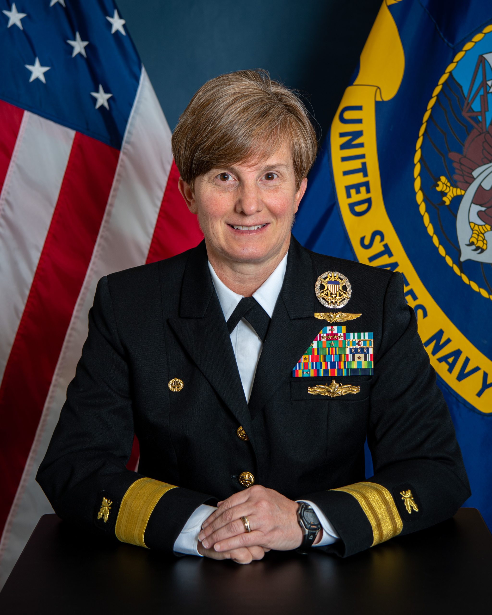 Portrait photo of Kristin Acquavella wearing her uniform against a backdrop of the United States and Naval flags.