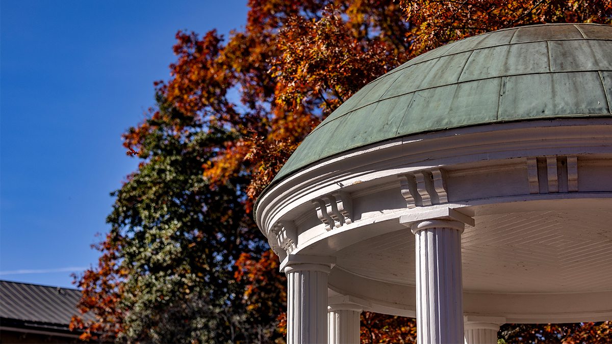 Close-up image of the Old Well on a sunny fall day on the campus of UNC-Chapel Hill with trees with orange leaves seen in the background.