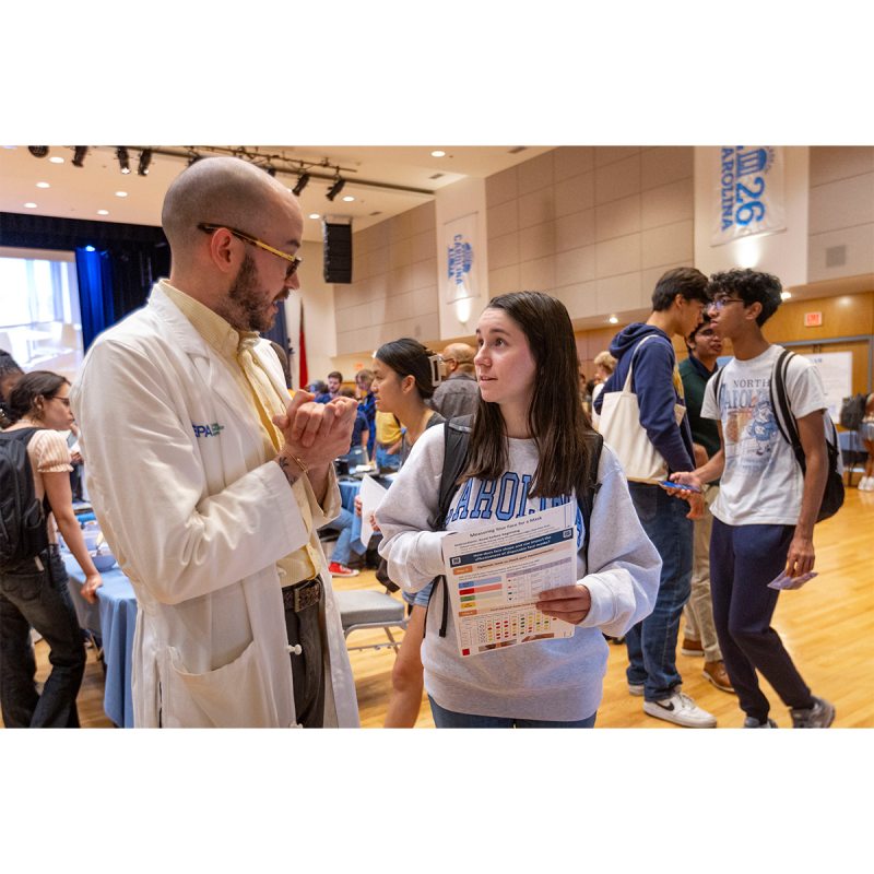 A student talking to an EPA researcher at a Research Week fair inside of a large hall on the campus of UNC-Chapel Hill.