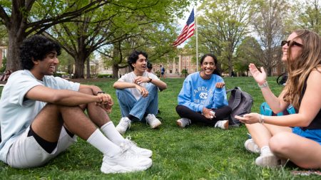 Four students talking and sitting on the lawn of McCorkle Place on the campus of UNC-Chapel Hill