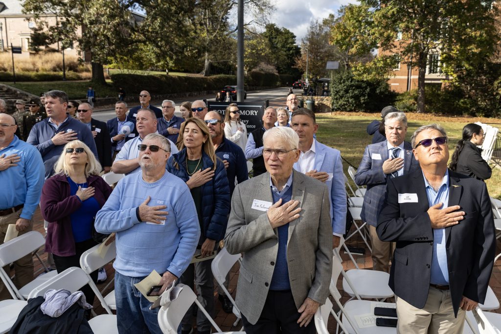 Group of people with their hands of the chest during the playing of the national anthem on the lawn of the Naval ROTC Armory on the campus of UNC-Chapel Hill.