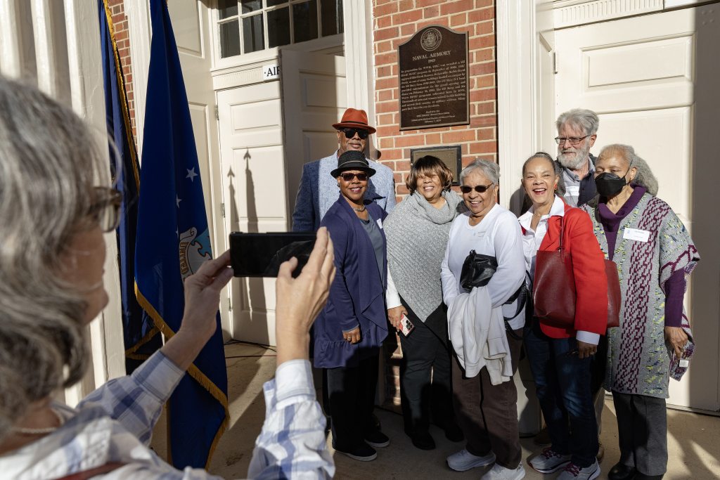 Descendants and friends of the original B-1 US Navy Band members posing for a group photo next to the historic marker outside the Naval ROTC Armory on the campus of UNC-Chapel Hill.