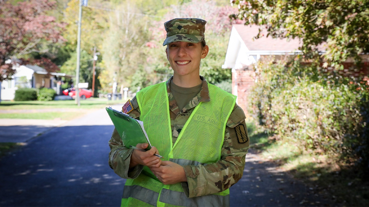 Jessica Bowling posing for a portrait in her National Guard uniform while holding a clipboard while walking around a neighborhood in Waynesville, N.C.