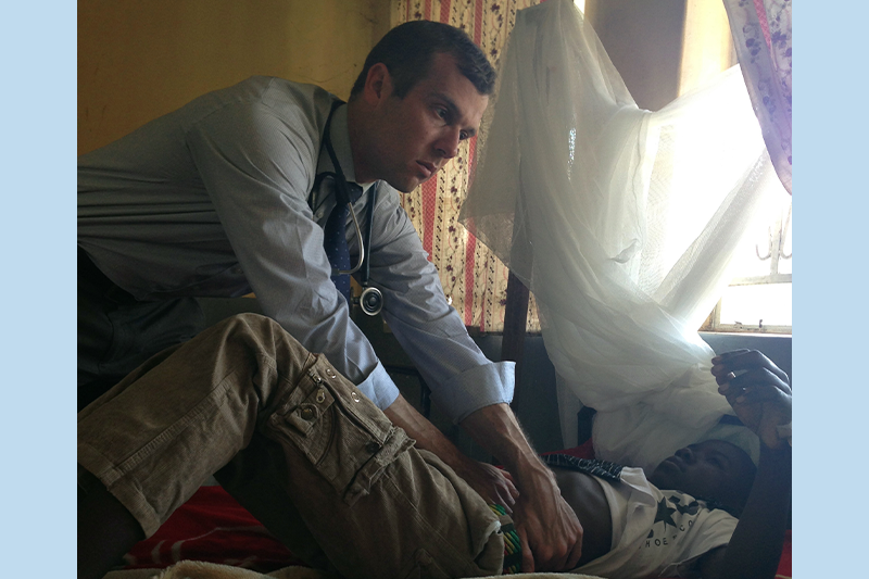 Dr. Ross Boyce tending to a child patient lying in a bed in Uganda.