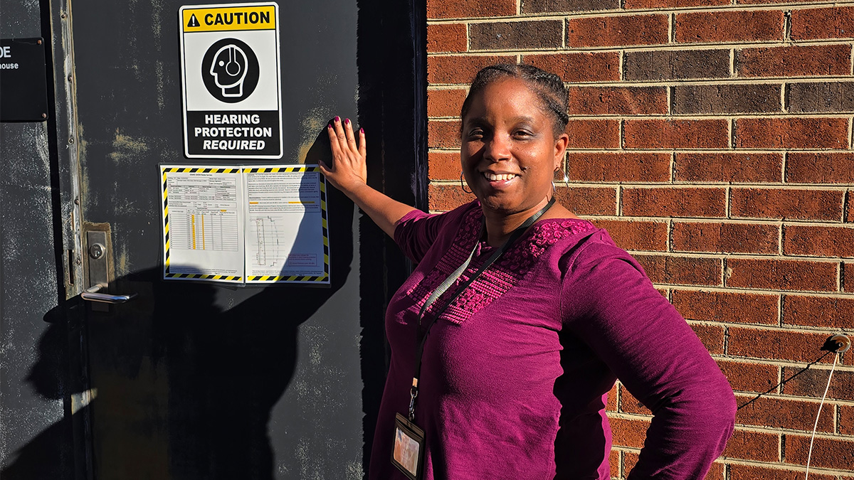 Portrait of Kim Haley outside of a building, posing next to a sign on a door that reads 