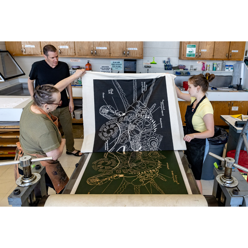 Bob Goldstein and Beth Grabowski helping a student hold off a large piece of art.