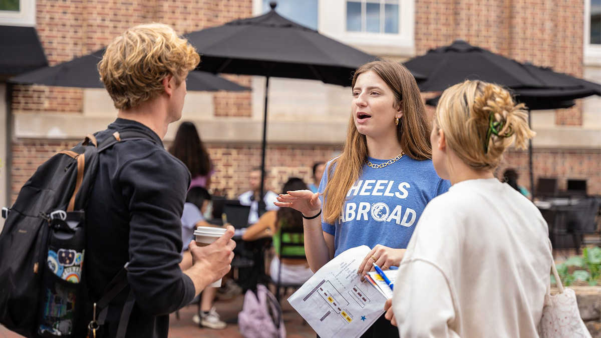 A student wearing a 'Heels Abroad' shirt discusses studying abroad with students.